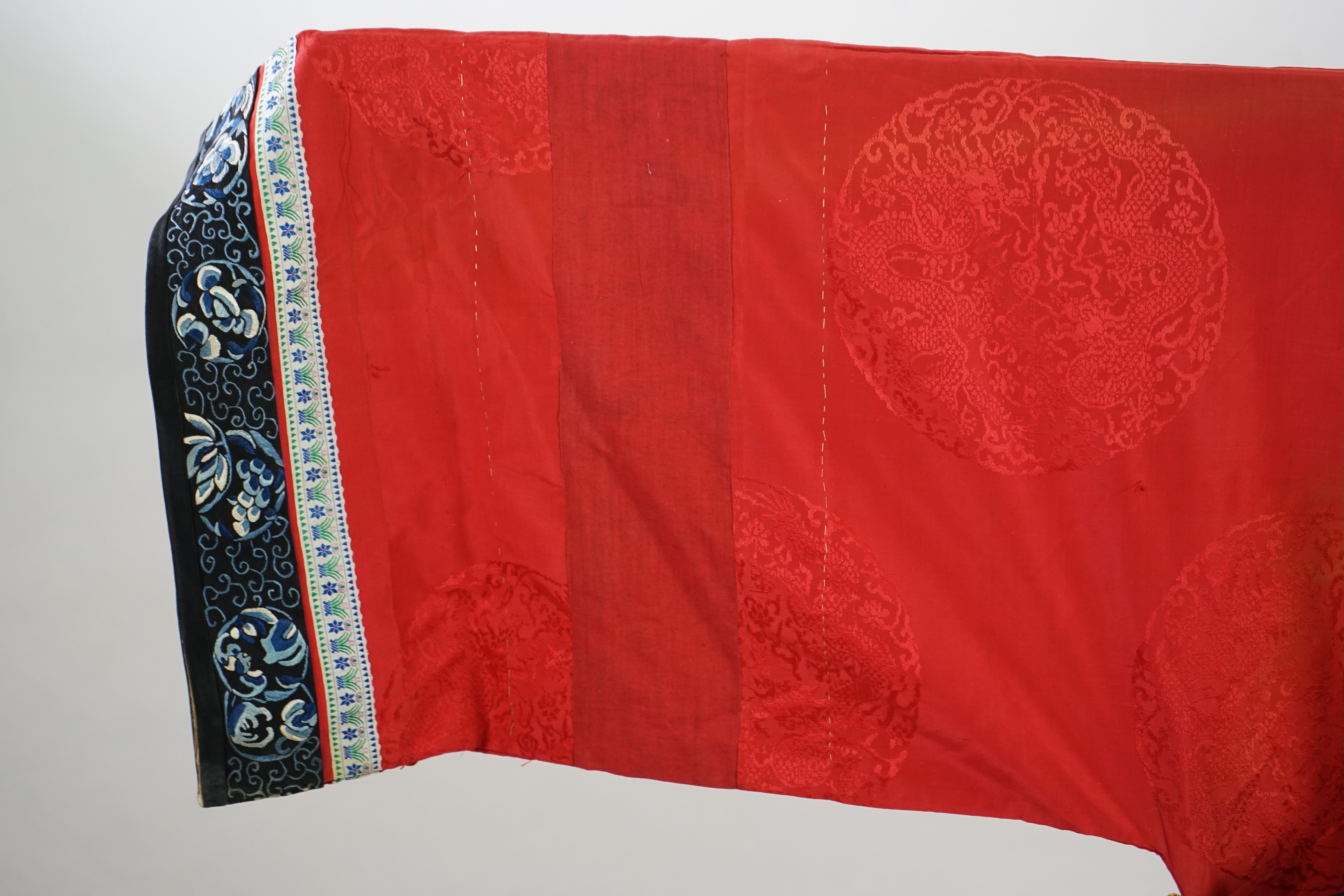 A late 19th century Chinese Manchu ladies red silk damask robe, with black and blue silk embroidered borders, ornately edged cream floral silk braiding, length from neck (back) to bottom edge 132cm long. Condition - stai